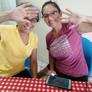 Two women hold their hand up to the camera while smiling during online training.